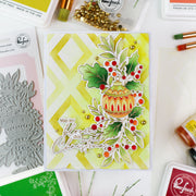 A handmade Christmas greeting card featuring a yellow and green chevron background, a die-cut ornament, holly leaves, red berries, and the phrase 'You are my Christmas' in white script. The card is styled on a white surface with crafting tools and brands like Perfect and Winchell visible around it.