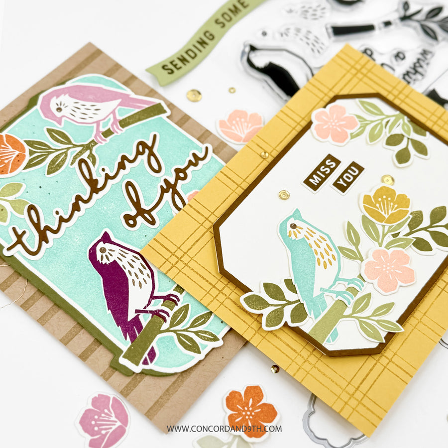 Two handmade greeting cards with bird and floral designs, displayed on a white background with scattered stickers and crafting tools. One card is kraft brown with a mint blue panel reading 'thinking of you,' and the other is mustard yellow with a white label panel reading 'miss you.