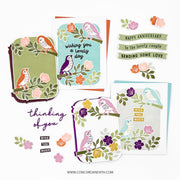 A flat lay of handmade greeting cards and matching stickers featuring colorful bird and floral illustrations. The cards include phrases like 'wishing you a lovely day,' 'HAPPY ANNIVERSARY to the lovely couple,' and 'thinking of you.