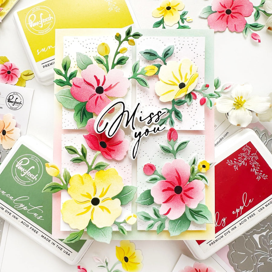 A floral greeting card with layered paper flowers and the words “Miss you” in script, surrounded by Ranger brand ink pads and craft tools on a white background.