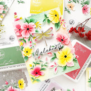 A handmade floral card with layered pink and yellow flowers, green leaves, a dragonfly embellishment, and the word 'Celebrate' in script, styled on top of other craft stamp and ink boxes from Handmade in Philadelphia.