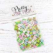 A clear plastic bag of decorative craft embellishments labeled 'Pretty Pink Posh' on a white wood background. The embellishments include pastel green, pink, blue, and white candy-shaped pieces. Pretty Pink Posh Gingerbread Cheer Clay Confetti