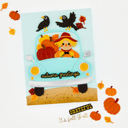 A handmade autumn-themed greeting card featuring a light blue pickup truck carrying a scarecrow with pumpkins, surrounded by layered paper fall leaves, pumpkins, and birds. The card is displayed on a white background with decorative scattered autumn elements.
