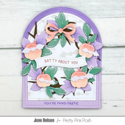 A handmade layered card featuring a lavender arched border, a white center, and a circular wreath design made from purple paper flowers, green leaves, peach-colored peaches, and brown branches. A white banner across the wreath reads 'BATTY ABOUT YOU', and the bottom border reads 'YOU'RE FANG-TASTIC'.