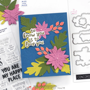 A handmade layered card with a blue background, pink flowers, green and yellow leaves, and orange berries, placed on top of stamp papers and metal stamp dies. The card reads, 'to know you is to love you.