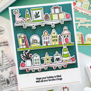 A handmade holiday greeting card featuring illustrated Christmas shelves with a deer, trees, gifts, houses, books, and ornaments, plus the printed phrase 'Hope your holiday is filled with all your favorite things.' The card is photographed on a styled flat-lay with other cards and stamp-related items around it.