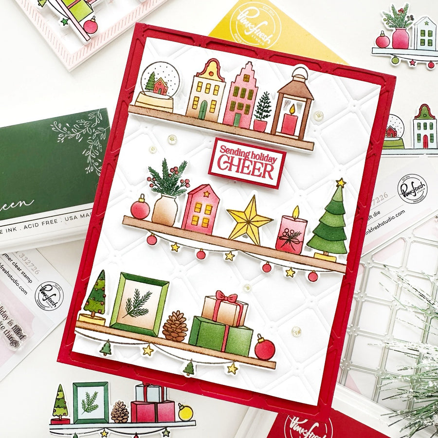 A handmade Christmas greeting card with a red border and layered holiday illustrations, displayed on a white background with stamps, envelopes, and other crafting supplies.
