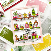 A festive handmade Christmas greeting card displayed on a styled flat-lay of crafting supplies. The card features colorful illustrated holiday shelves with houses, candles, a Christmas tree, books, gifts, a reindeer, and the text 'Wishing you a season to Treasure'.