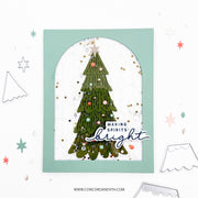 A handmade greeting card featuring a green Christmas tree with colorful ornaments and gold glitter inside an arched window frame, with the text 'MAKING SPIRITS bright' on a white background.