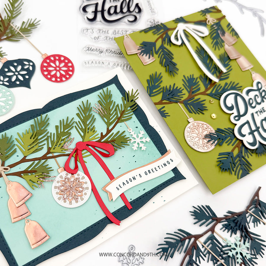 Two handmade layered Christmas greeting cards displayed on a white background with festive crafting props. One card is light aqua with green pine branches, copper bells, a red ribbon, and a white banner reading 'Season's Greetings.