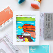 Colorful card with a paddle and scenic design on a white surface with craft supplies.