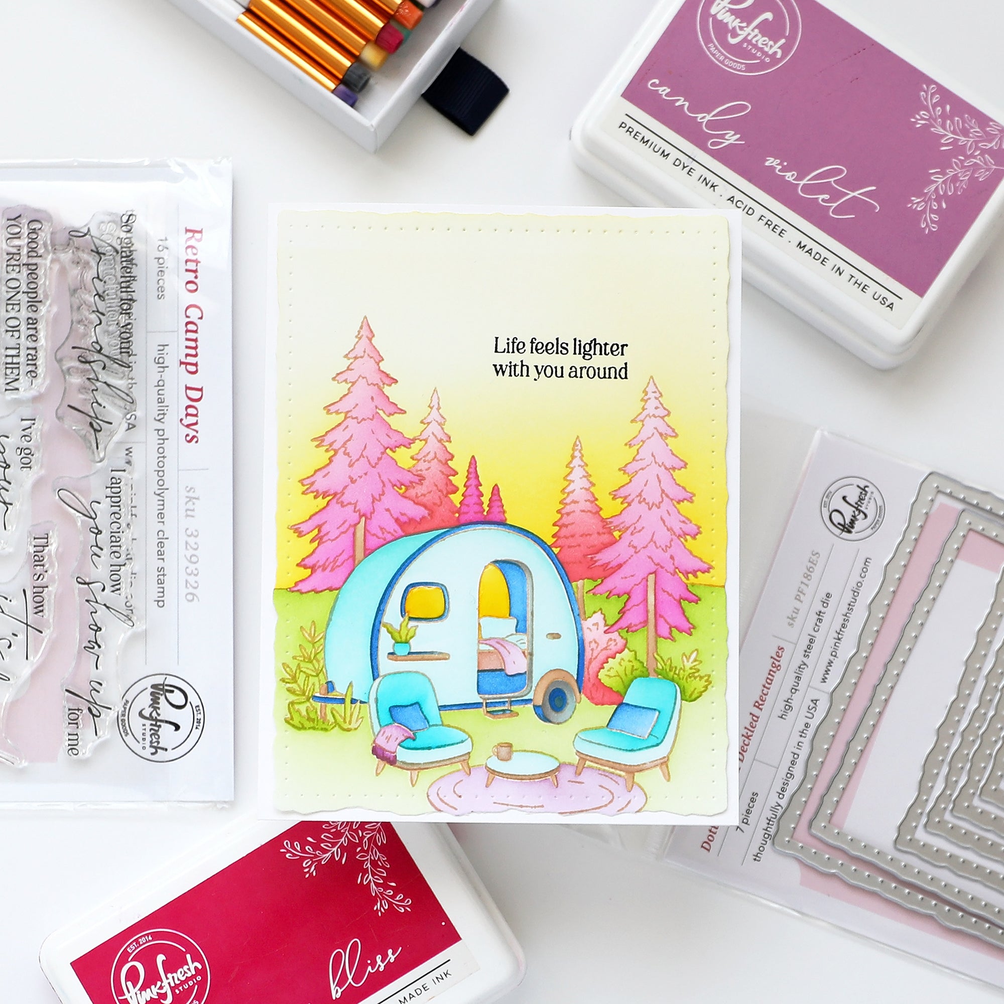 Colorful illustration of a camper with trees and text, surrounded by stamping supplies on a white background.