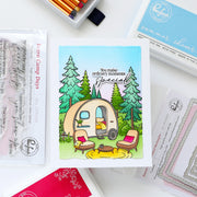 A handmade greeting card featuring a camping trailer in a forest with the text 'You make ordinary moments special', surrounded by crafting tools and branded packaging from Paper Hearts.
