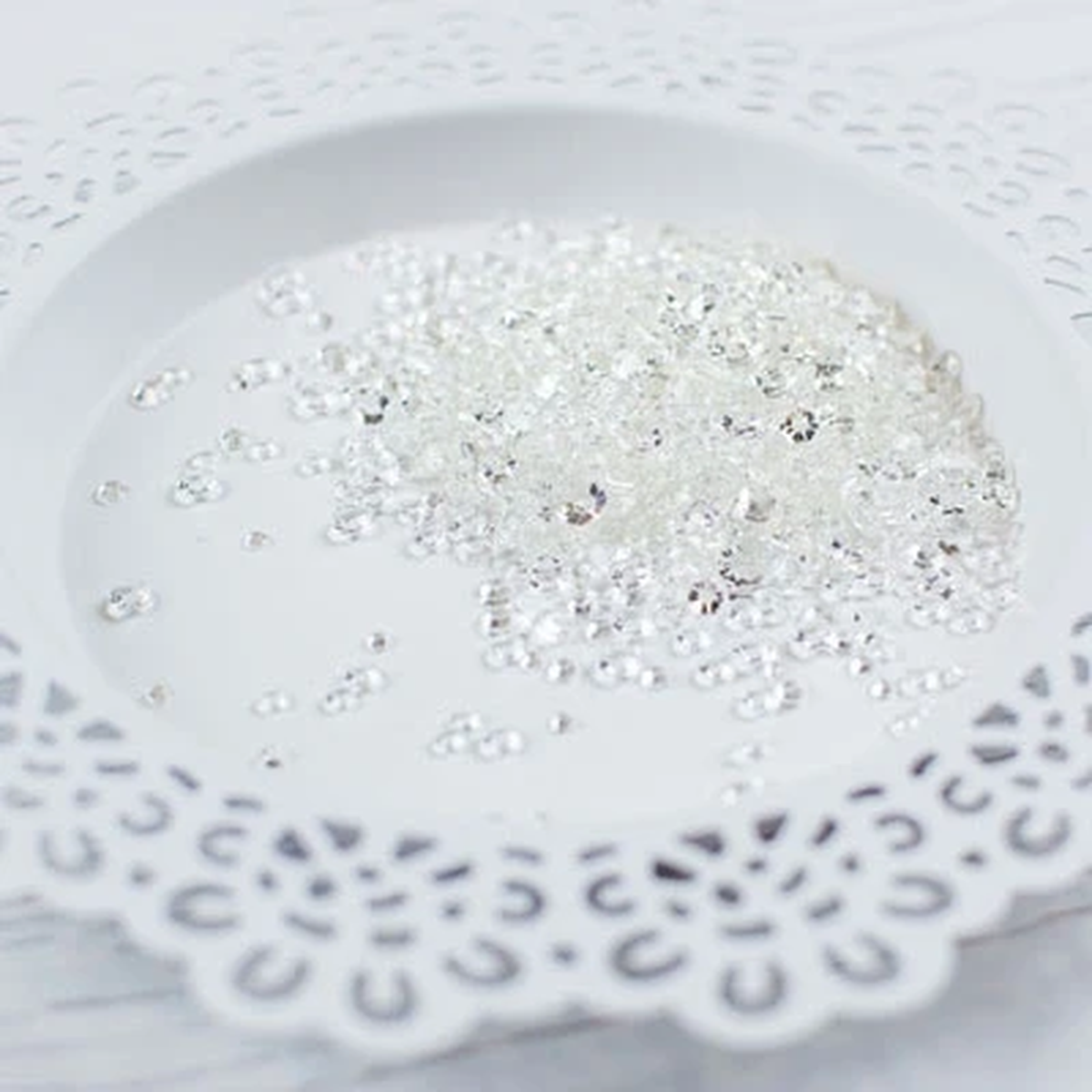 Clear rhinestone craft embellishments scattered on a white ceramic plate with a scalloped cutout edge. Pretty Pink Posh Sparkling Clear Jewels