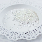 Clear rhinestone craft embellishments scattered on a white ceramic plate with a scalloped cutout edge. Pretty Pink Posh Sparkling Clear Jewels