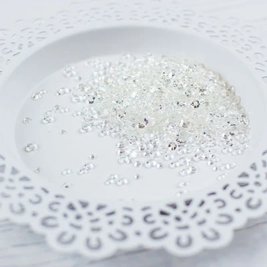 Clear rhinestone craft embellishments scattered on a white ceramic plate with a scalloped cutout edge. Pretty Pink Posh Sparkling Clear Jewels