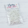 A clear plastic bag filled with many small clear rhinestones or crystal embellishments, attached to a white paper header card that reads 'Pretty PINK POH' in dark script and pink block letters. The package is photographed on a white wood surface. Pretty Pink Posh Sparkling Clear Jewels