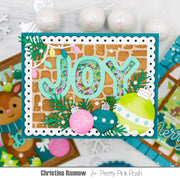 A handmade Christmas greeting card featuring the word 'JOY' in layered mint green letters filled with multicolored confetti, decorated with green pine branches, a pink ornament, a lime green ornament, and a white scalloped border. The card is displayed on a white surface with holiday-themed props in the background, and text at the bottom reads 'Christina Rannow for Pretty Pink Posh'.