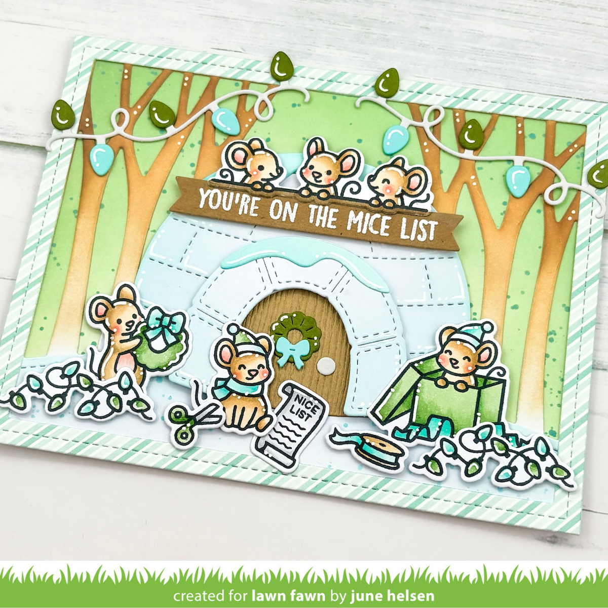 A handmade holiday card featuring cute cartoon mice around an igloo house, with the text 'YOU'RE ON THE MICE LIST' and small decorative details like ornaments and a wreath, photographed on a light wood background.