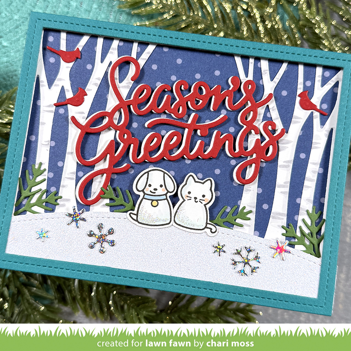 Handmade greeting card featuring a snowy hill with a cat and dog die cut stamped images. There are trees in the background on a blue background with white dots.