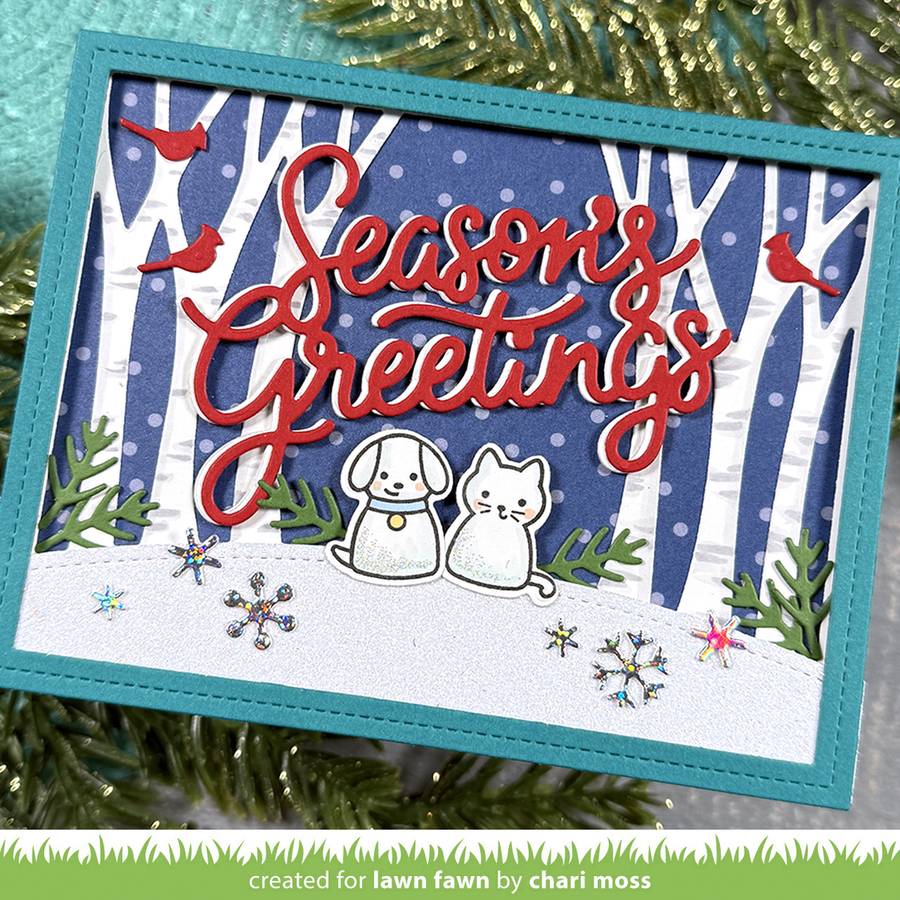 Handmade greeting card featuring a snowy hill with a cat and dog die cut stamped images. There are trees in the background on a blue background with white dots.