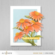 A handmade greeting card featuring layered orange daisy-like flowers with yellow centers, green leaves, and a yellow banner reading 'YOU'VE GOT THIS!'. The card is displayed on a light gray wood-textured background, with 'ALTENEW' and 'LYDIA EVANS DESIGN TEAM' visible at the bottom. Altenew Craft-A-Flower: Coneflower Layering Die Set card ideas