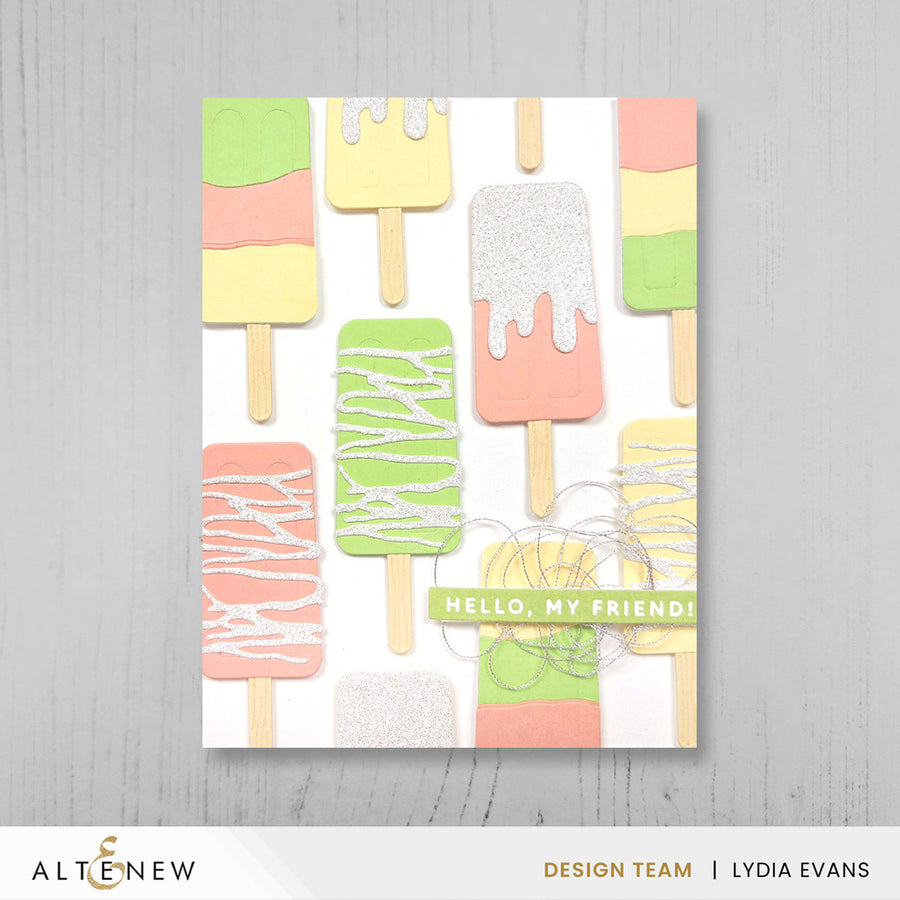 A handmade greeting card featuring a playful pattern of colorful popsicle sticks on a white background, with the text 'HELLO, MY FRIEND!' across the center. The print is shown against a light gray wood-textured background, with branding at the bottom reading ALTNEW and DESIGN TEAM | LYDIA EVANS. Altenew Mini Delight: Sweet Popsicles Stamp & Die Set card ideas