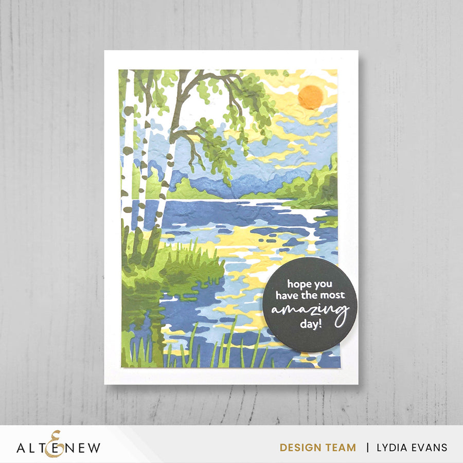 A handmade greeting card featuring a watercolor-style lakeside landscape with birch trees, blue water, green grass, and a yellow sun. A dark circular sticker on the print reads, 'hope you have the most amazing day!'. Altenew Craft Your Life Project Kit: Painterly Perfection card ideas