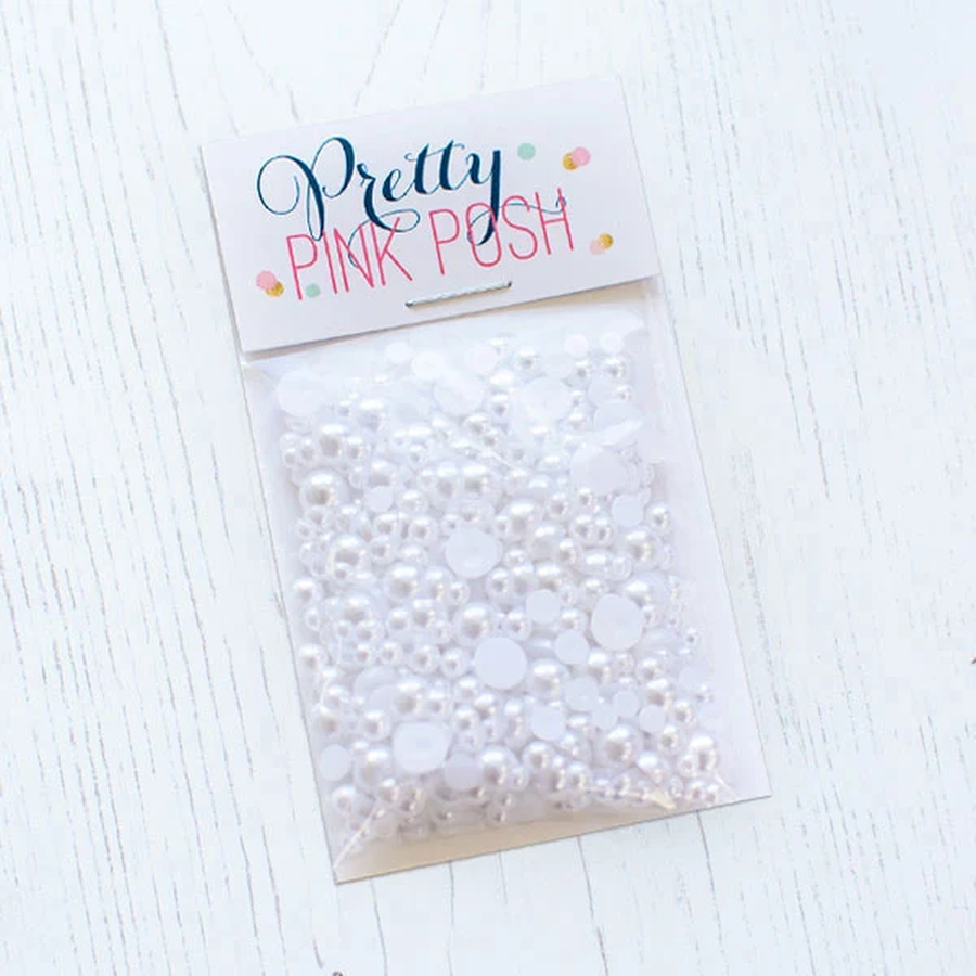 A clear plastic bag of white faux pearls, sealed with a white header card that reads 'Pretty PINK POSH' in blue and pink lettering, placed on a white wood surface. Pretty Pink Posh Marshmallow Pearls