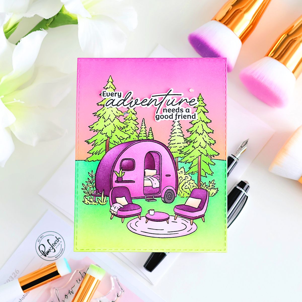Colorful card with a purple camper and trees, surrounded by stationery items on a white background.