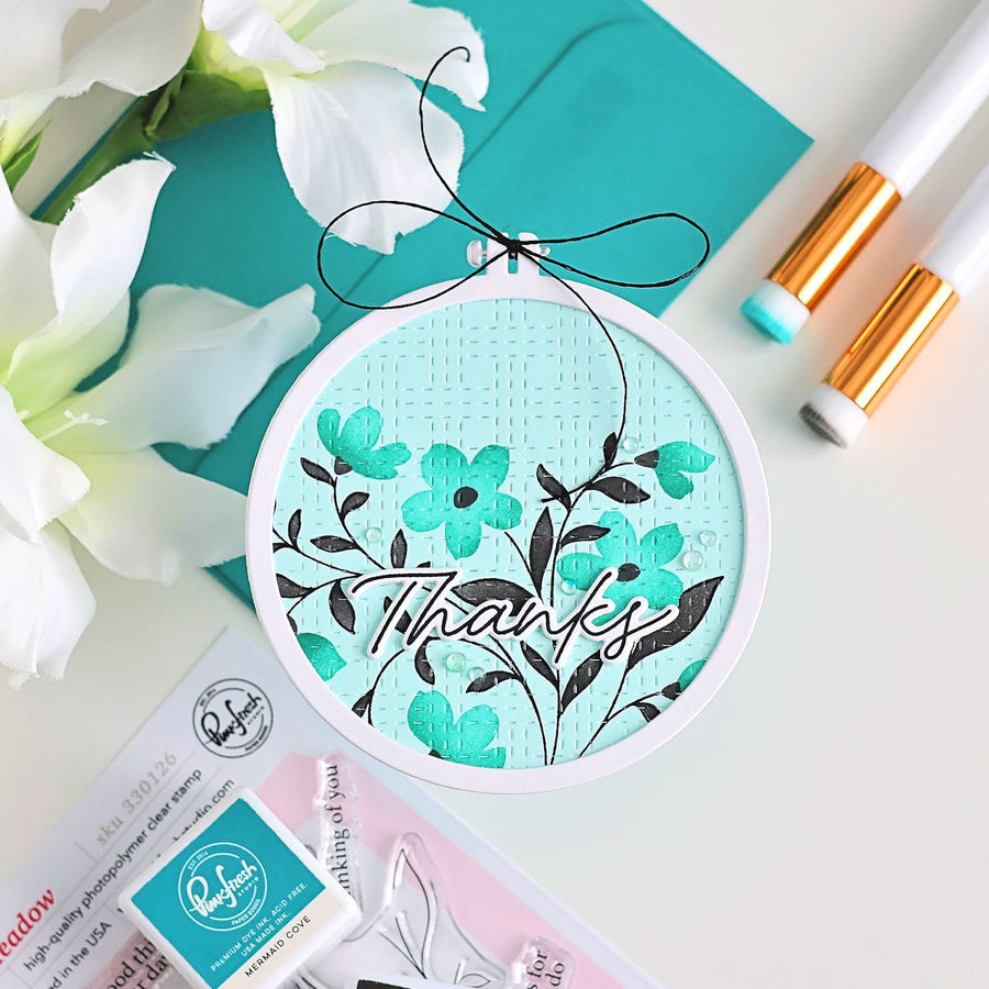 Embroidery hoop with floral design and 'Thanks' text on a white background with flowers and stationery items.