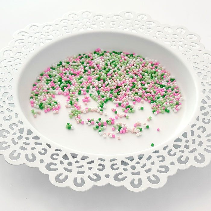 Pink, green, and white craft sprinkles scattered in the center of a white ceramic plate with a scalloped edge. Pretty Pink Posh Mistletoe Kisses Shaker Beads