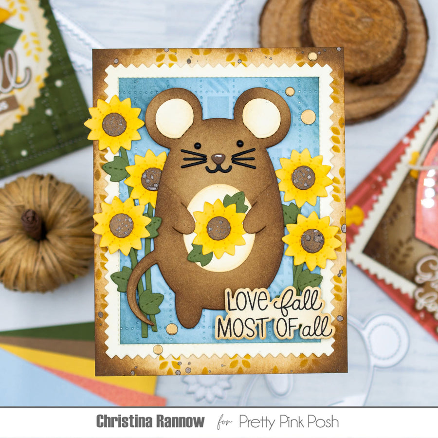 A handmade autumn-themed greeting card featuring a brown mouse holding yellow sunflowers, with the text 'Love fall MOST OF all'. The card is displayed on a light blue surface with craft props and a brand watermark at the bottom.