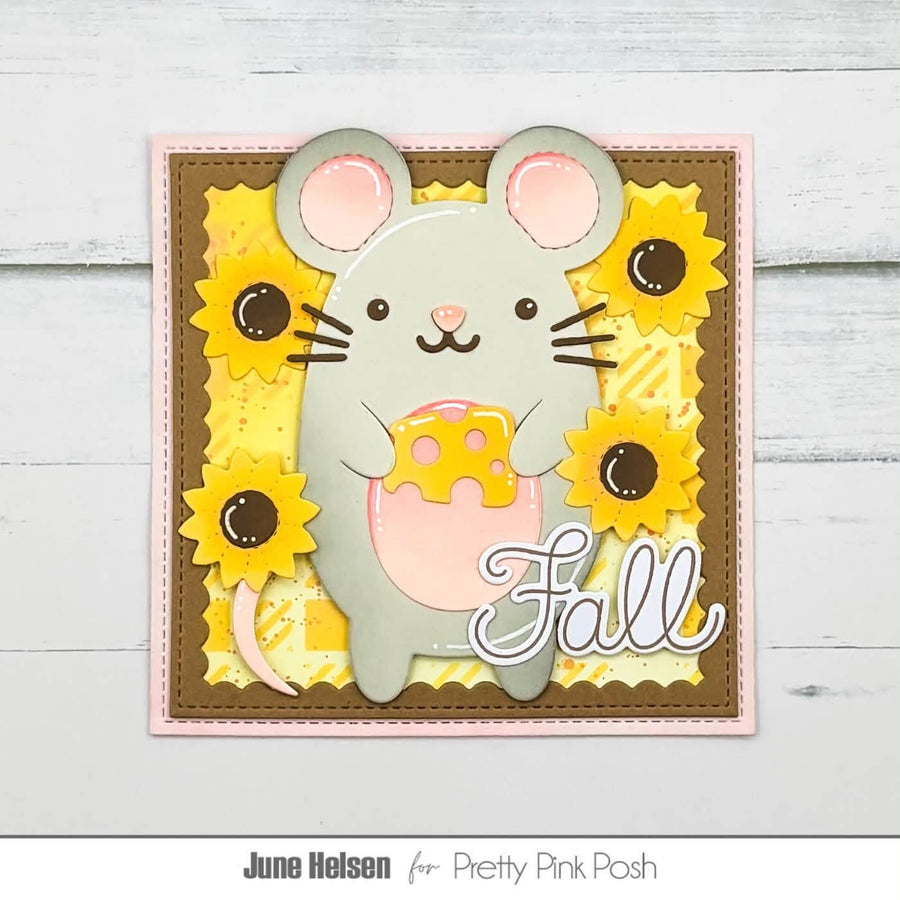 A handmade autumn-themed card featuring a gray mouse holding a yellow cheese wedge, surrounded by yellow sunflowers and the word 'Fall' in white script. The card is displayed on a light gray wood background with a white border at the bottom containing the text 'June Helsen for Pretty Pink Posh'.
