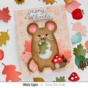 A handmade layered card featuring a cute brown mouse holding a green leaf, surrounded by pink and orange autumn leaves, a red mushroom, and the words 'many thanks' at the top. The card is displayed on a white surface decorated with matching autumn leaves, with the text 'Mindy Eggen for Pretty Pink Posh' at the bottom.