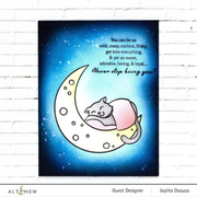 A handmade greeting card featuring a sleeping gray cat curled up inside a pale yellow crescent moon on a starry blue night sky. White script text appears near the top right, and the print is shown hanging against a white brick wall. Black print stamped with Altenew Obsidian Pigment Ink