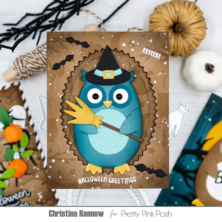 A handmade Halloween greeting card featuring a blue owl wearing a black witch hat and holding a broom, surrounded by a brown scalloped frame with bats and falling leaves. The card is styled in a flat-lay with autumn props including a small pumpkin, twine, and other cards.