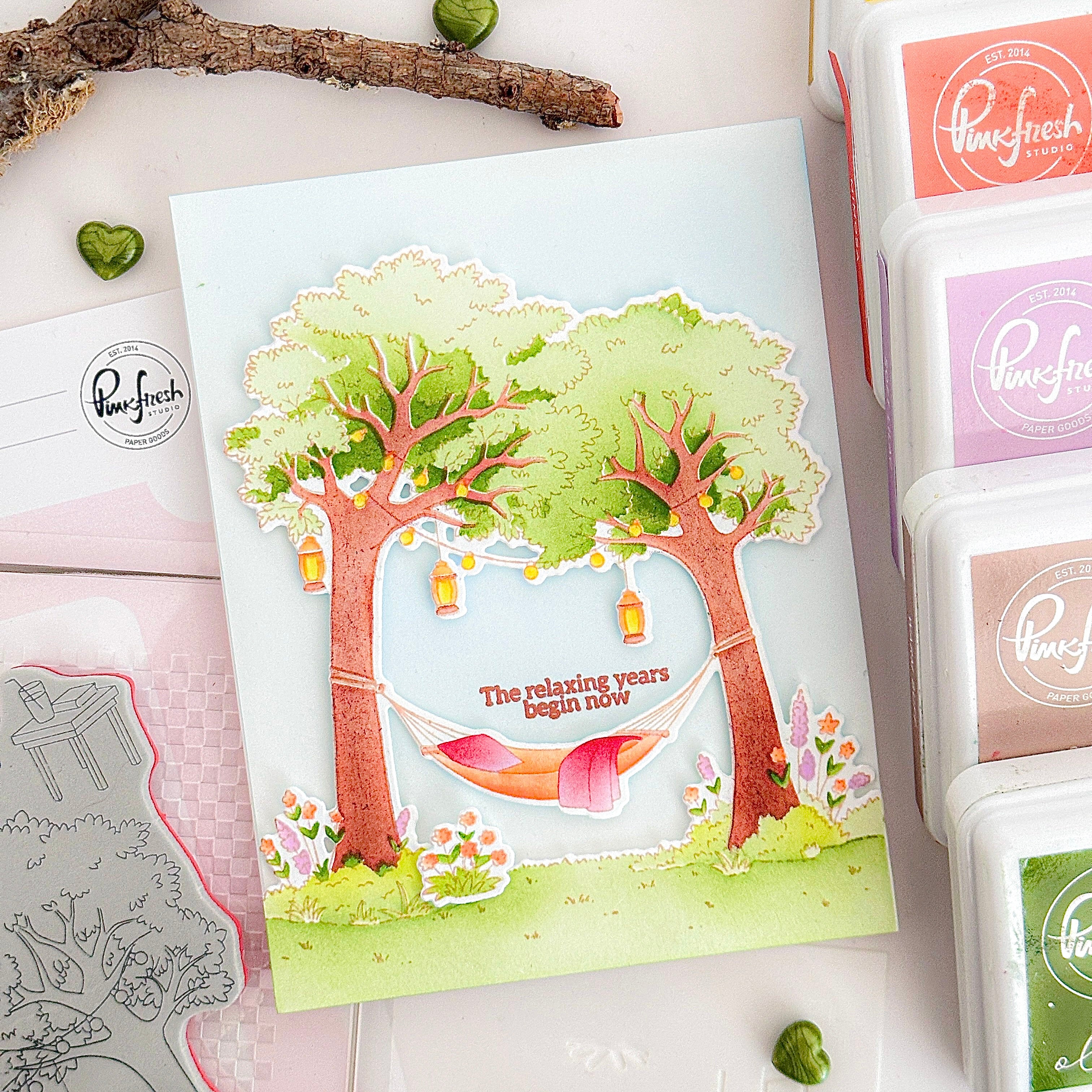 Card with tree and hammock design surrounded by Pinkfresh Studio products on a white surface