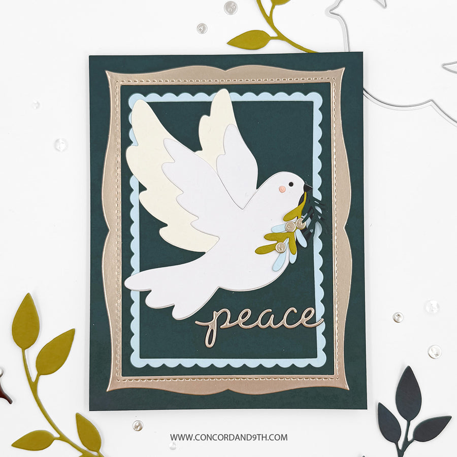 A handmade layered greeting card featuring a white dove holding an olive branch, with the word 'peace' in metallic script at the bottom. The card has a dark teal background, a beige inner border, and a light blue scalloped inner frame, styled on a white background with decorative leaf cutouts.