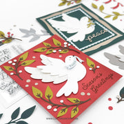 Two layered handmade Christmas greeting cards displayed on a white background. The front card is red with a white dove, green and gold leaves, and the words 'Season's Greetings' and 'Peace'.
