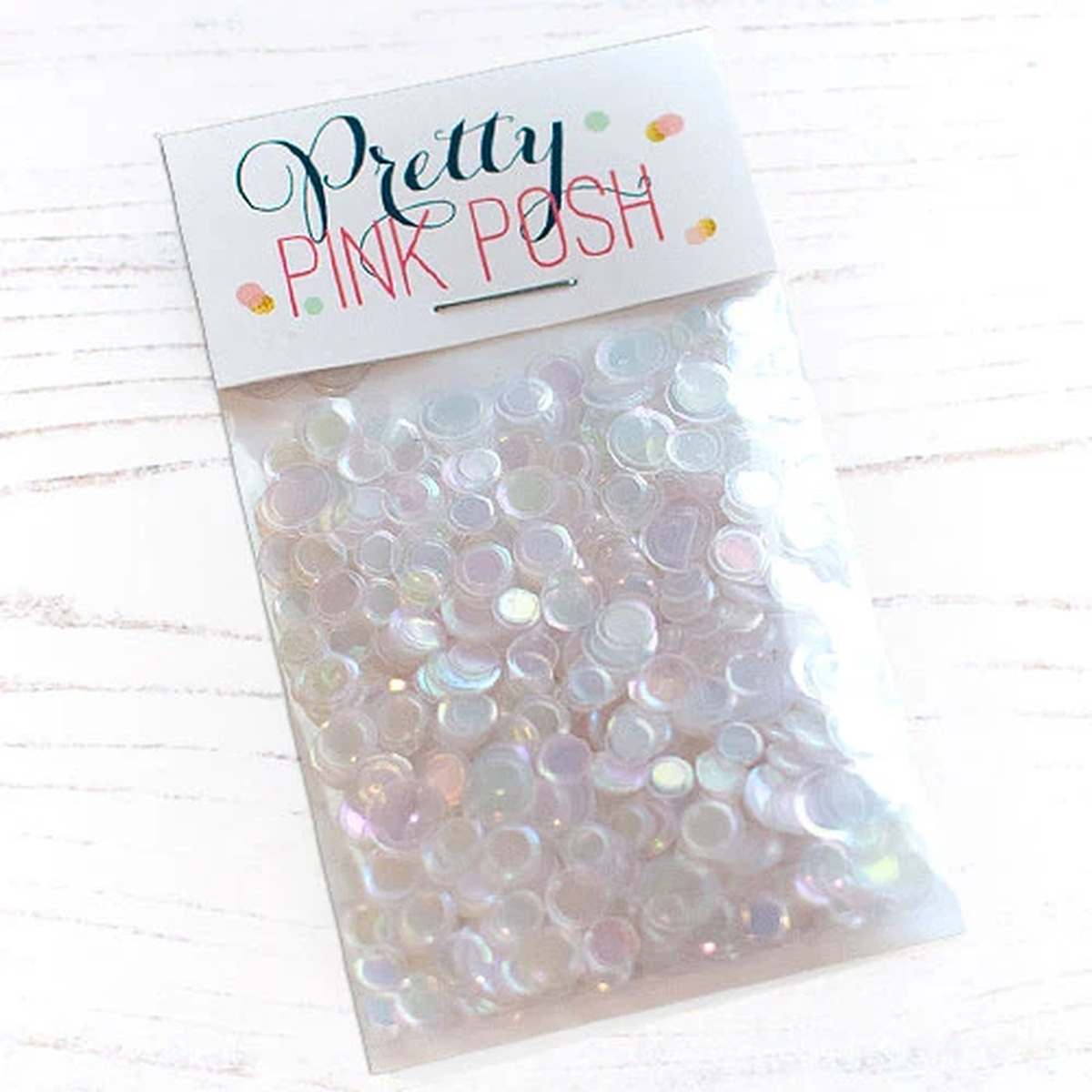 A clear plastic bag filled with small iridescent round embellishments, sealed with a white header card that reads 'Pretty Pink Posh' on a light wood background. Pretty Pink Posh Pearl Prism Confetti Mix
