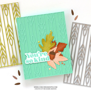 A handmade greeting card with a mint green embossed wheat pattern, decorated with layered autumn leaves, an acorn, and a die-cut sticker that reads 'You're so kind'. Two metal die-cutting mats are partially visible on either side on a white background.