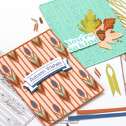 Two handmade greeting cards displayed on a white background, one with a peach and brown striped pattern and blue-green leaf motifs reading 'Autumn Wishes,' and the other in mint green with embossed leaf texture and layered autumn leaves reading 'You're so kind.' Crafting tools and paper scraps are visible around them.