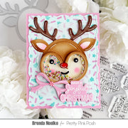 A handmade Christmas greeting card featuring a reindeer face with antlers, a pink bow, and the phrase 'Have a Joyful Christmas' on a pastel star-patterned background, styled with white flowers and holiday-themed stamps.