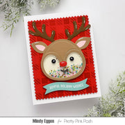 A handmade holiday greeting card featuring a reindeer face with brown antlers, a red nose, and colorful glitter in the eyes, set on a red patterned background with a teal banner reading 'Joyful Holiday Wishes'.