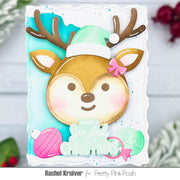 A handmade Christmas greeting card featuring a cute cartoon reindeer face with brown antlers, a mint green Santa hat, and a pink bow. The card has a scalloped white border, a light blue background, and includes the text 'HAVE A joyful CHRISTMAS' along with pink and mint ornaments.
