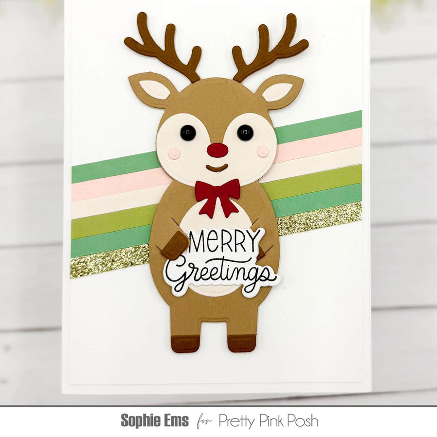 A handmade Christmas greeting card featuring a cute layered paper reindeer with brown antlers, a red bow, and a white belly that says 'Merry Greetings' in script. The reindeer stands in front of pastel green, pink, and light green horizontal stripes with a glittery gold accent stripe.