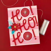 A handmade red and pink striped greeting card with layered red 'Ho Ho Ho!' letters, floral embellishments, and circular starburst decorations, shown on a red background with a spool of thread nearby.