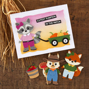 A handmade felt craft card featuring a raccoon pulling a wagon with pumpkins, with the text 'CUTEST PUMPKIN IN THE PATCH,' displayed on a wooden surface with decorative wheat and small felt animal cutouts below.