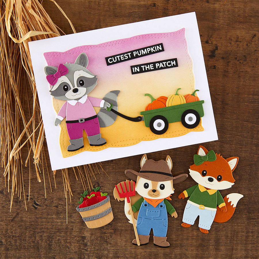 A handmade felt craft card featuring a raccoon pulling a wagon with pumpkins, with the text 'CUTEST PUMPKIN IN THE PATCH,' displayed on a wooden surface with decorative wheat and small felt animal cutouts below.